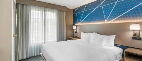 A hotel room with a large bed, a desk, a phone, and a wall with geometric patterns.