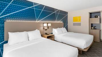 Habitación de hotel con dos camas, una mesita de noche, una lámpara de pared y un estante con un hervidor.