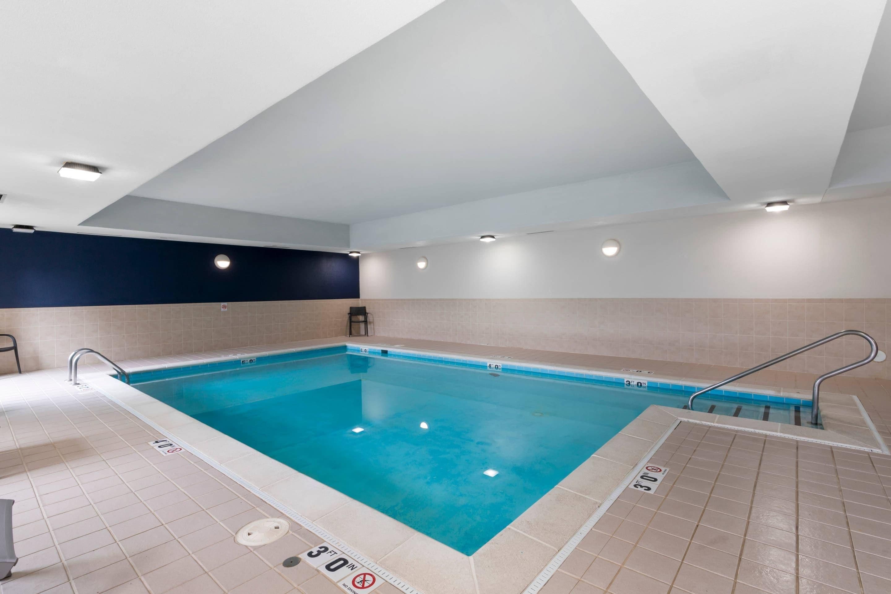 Una piscina interior con agua cristalina, paredes enlosadas e iluminación empotrada en el techo.