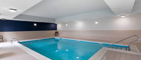 Una piscina interior con agua cristalina, paredes enlosadas e iluminación empotrada en el techo.