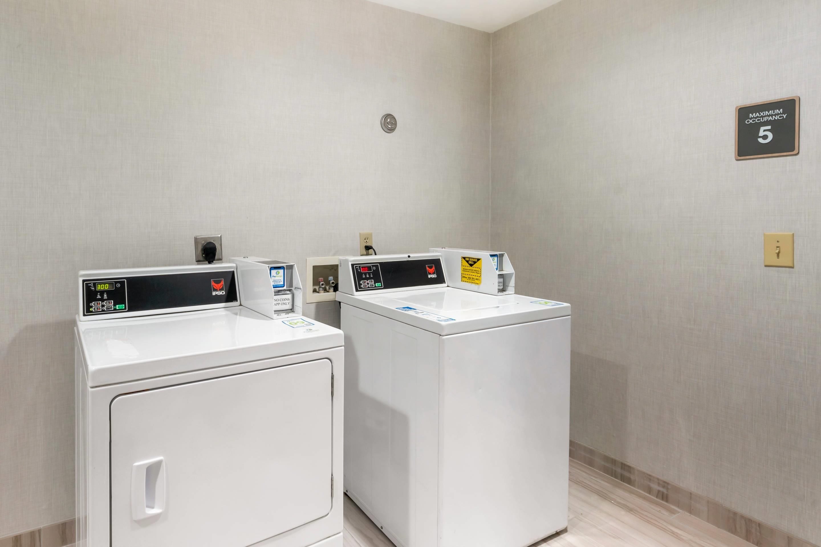 Une buanderie d'hôtel équipée de deux machines à laver à chargement frontal, d'un panneau indiquant « Nombre maximal d'utilisateurs : 5 » et d'un autre panneau indiquant « Pour les interventions de maintenance ».