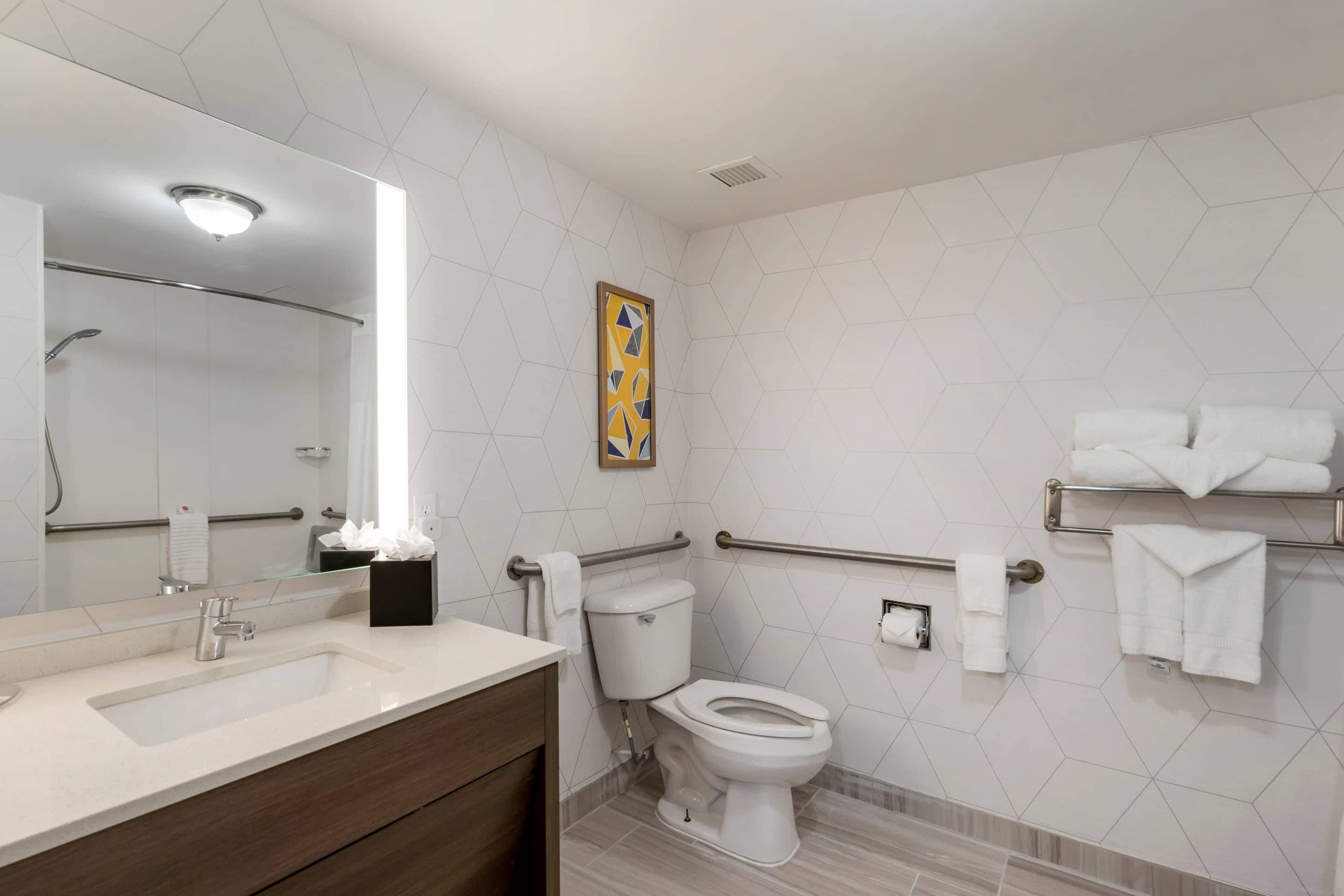 A modern bathroom with a large mirror, a toilet, a shower area, and a vanity with a sink.