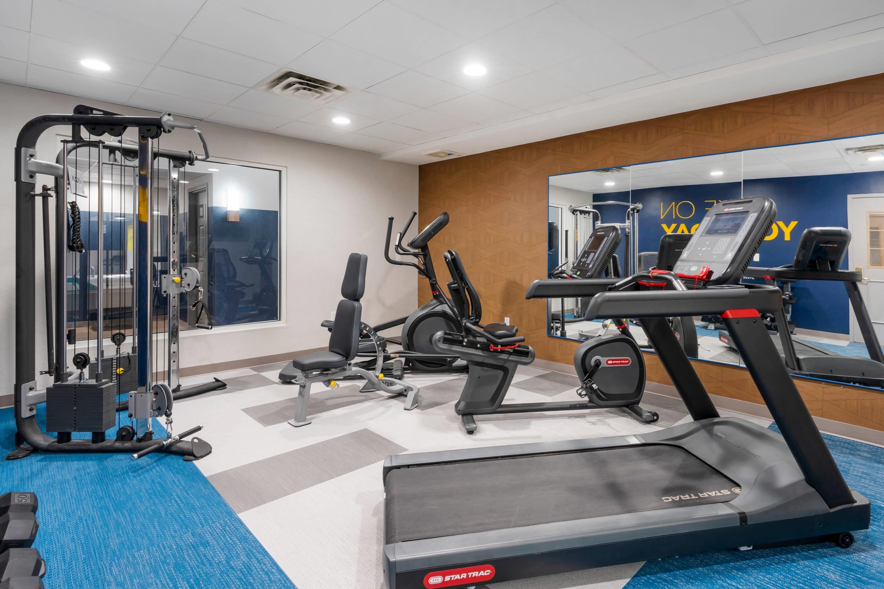 A gym with cardio equipment, weight machines, and a mirrored wall.