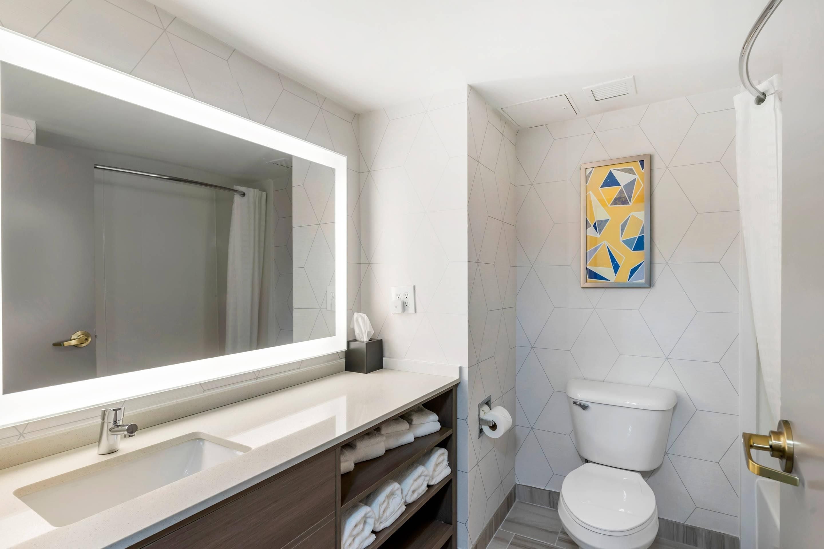 A modern bathroom with a large mirror, a sink, a toilet, and a towel rack.