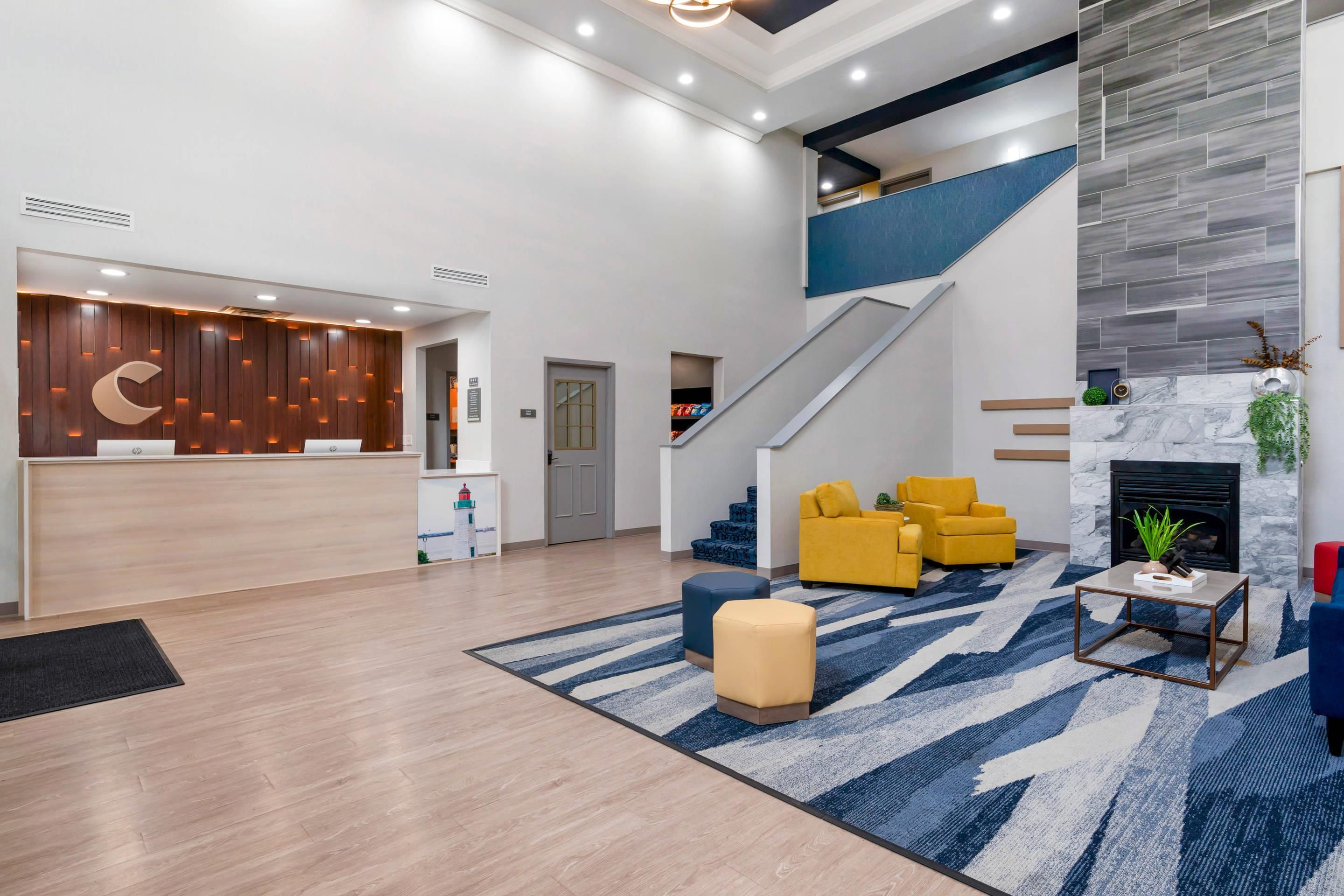 A modern lobby with a reception desk, seating area, staircase, and a fireplace.
