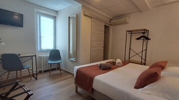 Una habitación de hotel con cama, escritorio, silla, radiador y ventana.