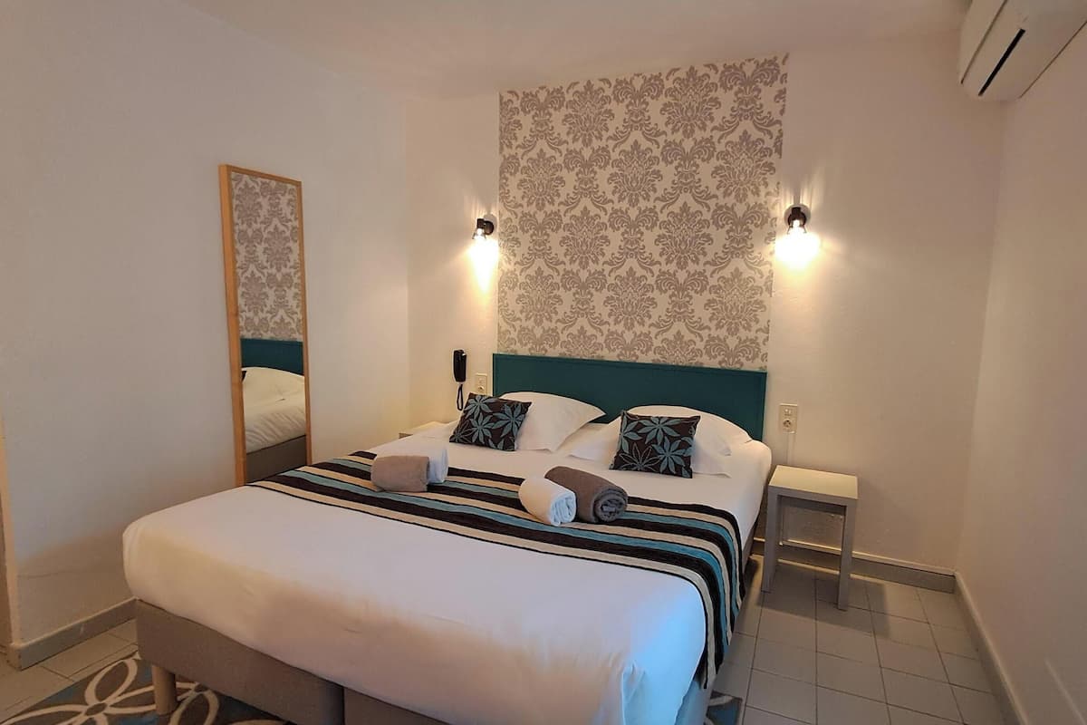 A hotel room with a large bed, a mirror, two bedside lamps, and a patterned wallpaper.