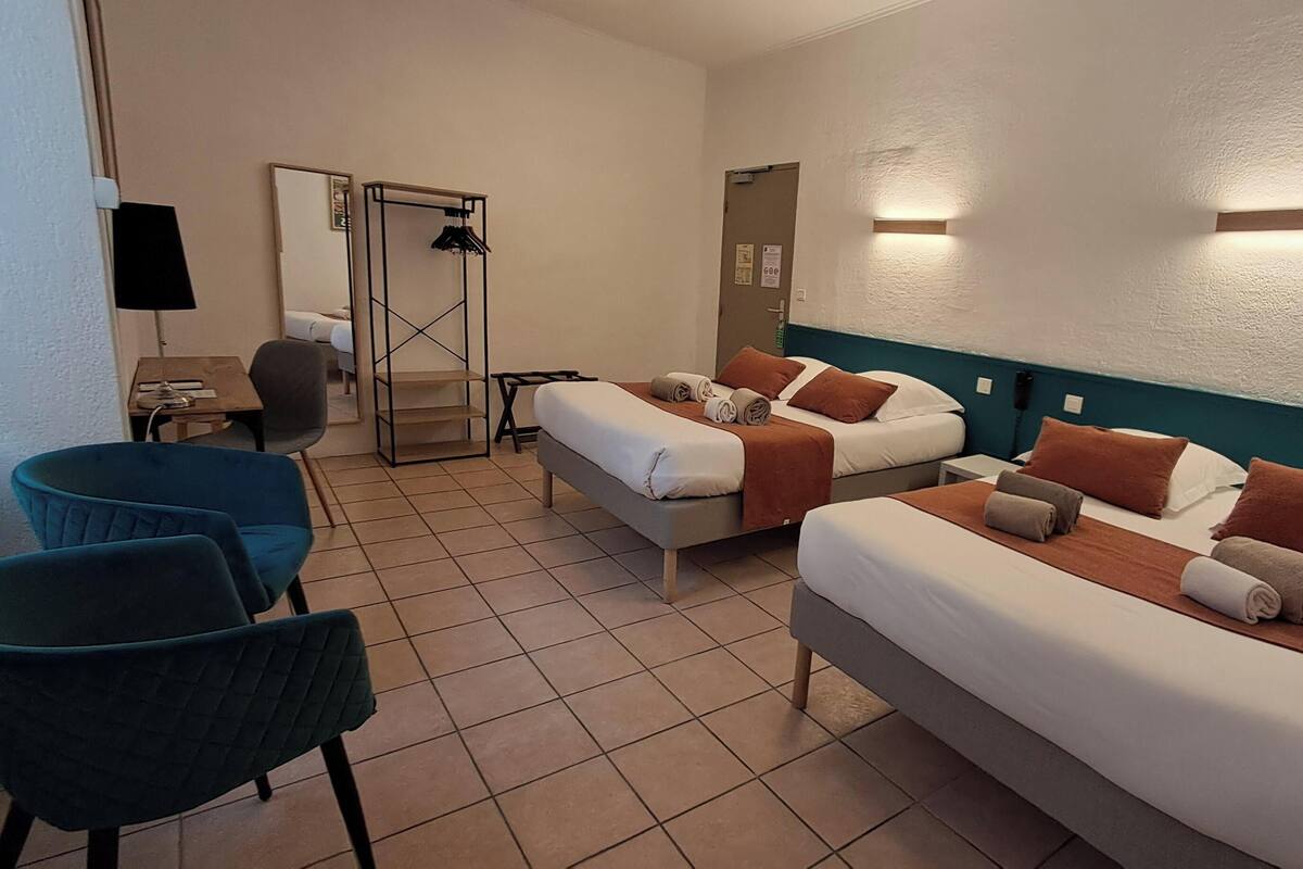 A hotel room with two beds, a desk, a chair, and a wardrobe.