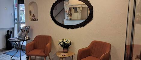 Una habitación con dos sillones anaranjados, una mesita con un florero y un espejo grande en la pared.