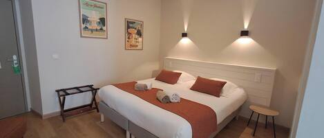 Una cama bien hecha con cabecera, dos lámparas de pared y un taburete pequeño.
