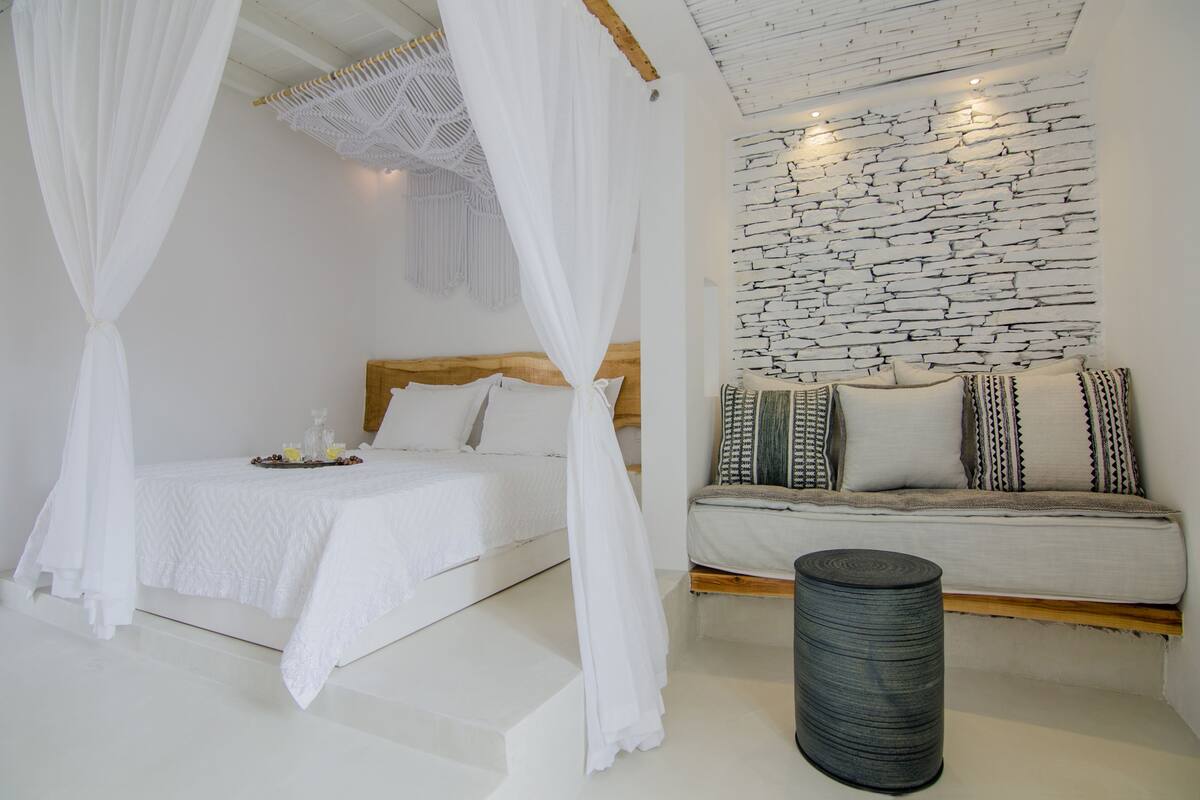 Un dormitorio con cama, sofá, pared con textura y una pequeña mesa redonda.