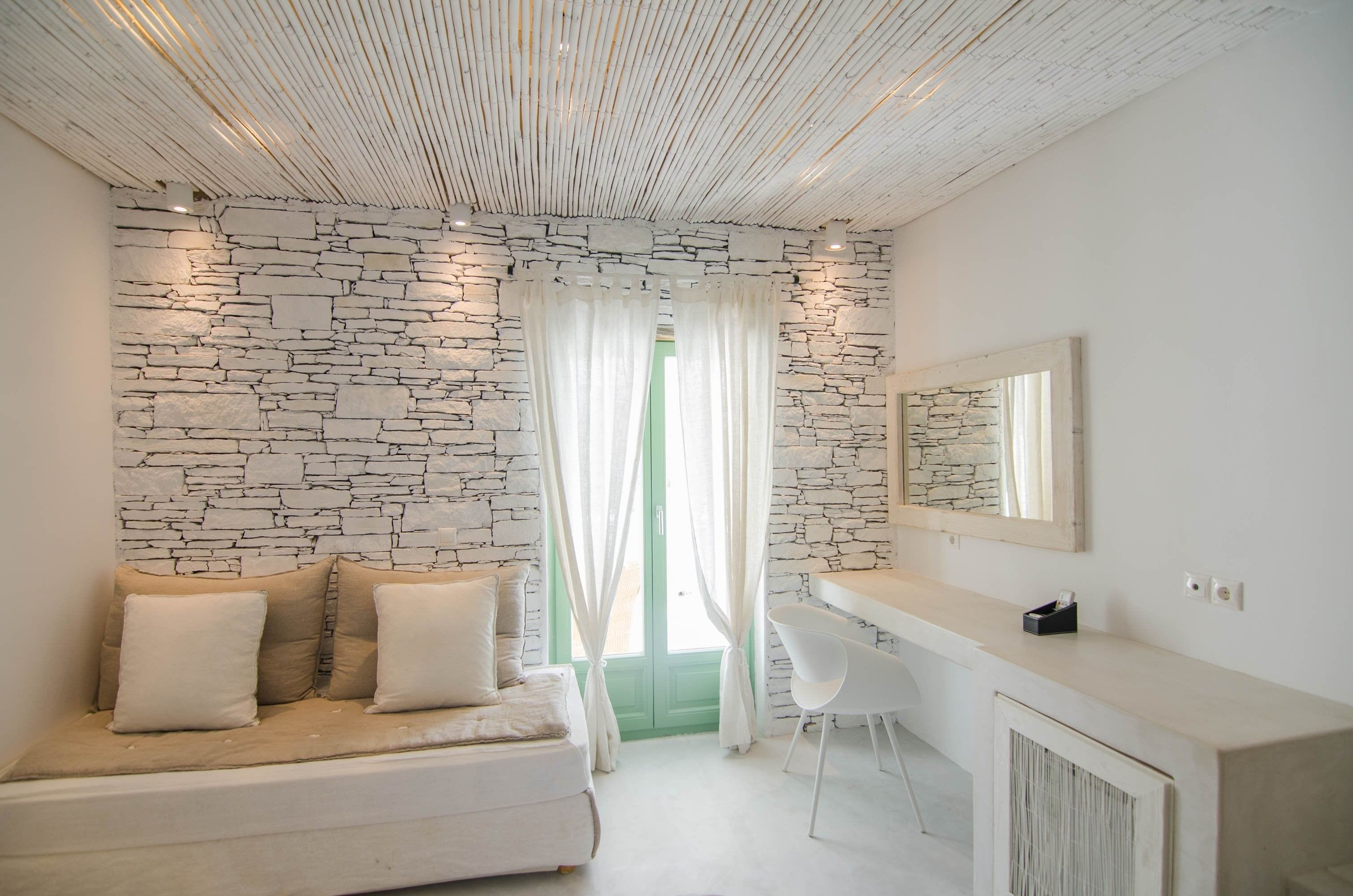 A modern room with a stone wall, a white sofa with cushions, a white desk, and a mirror.