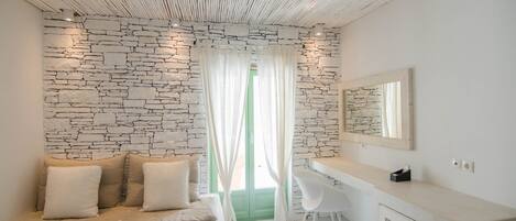 A modern room with a stone wall, a white sofa with cushions, a white desk, and a mirror.