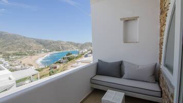 A balcony with a white wall, a gray cushioned bench, and a view of a beach and ocean.