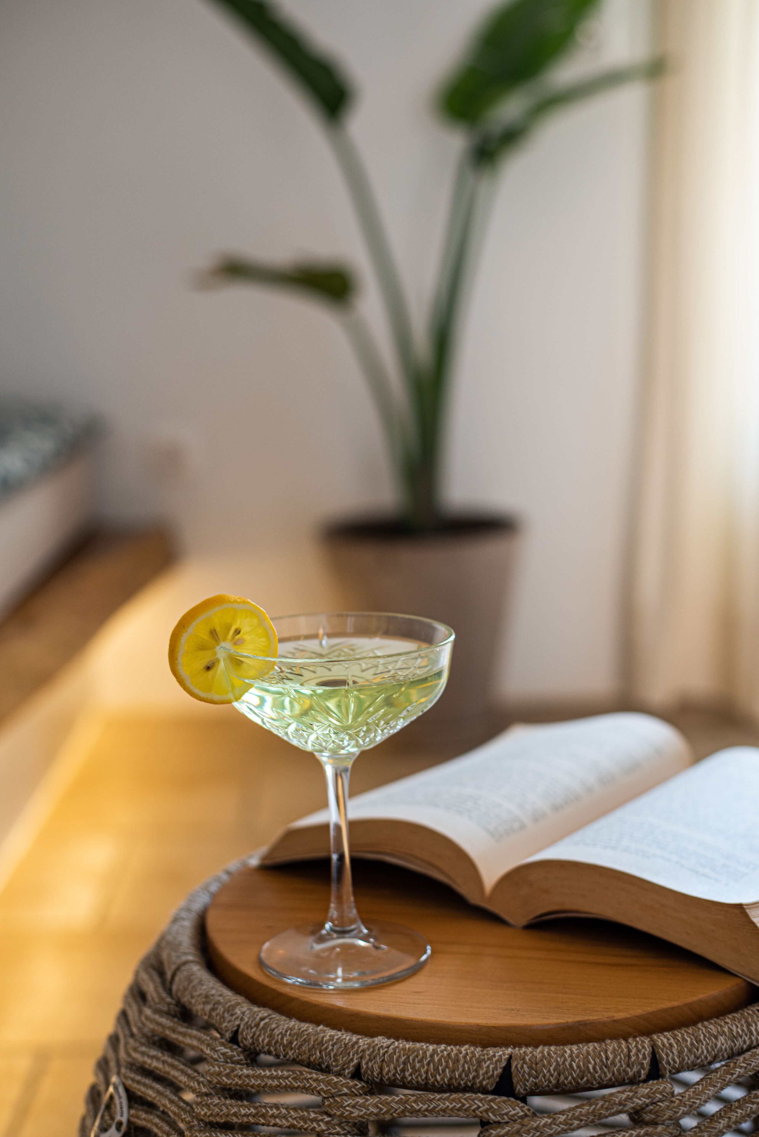 Een helder glas met een citroenpartje op een houten tafel, een open boek ernaast en een kamerplant op de achtergrond.
