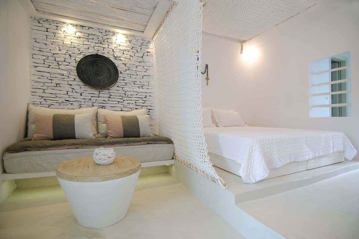 Un dormitorio con pared de piedra, una cama, un sofá con cojines y una pequeña mesa redonda con un objeto decorativo.