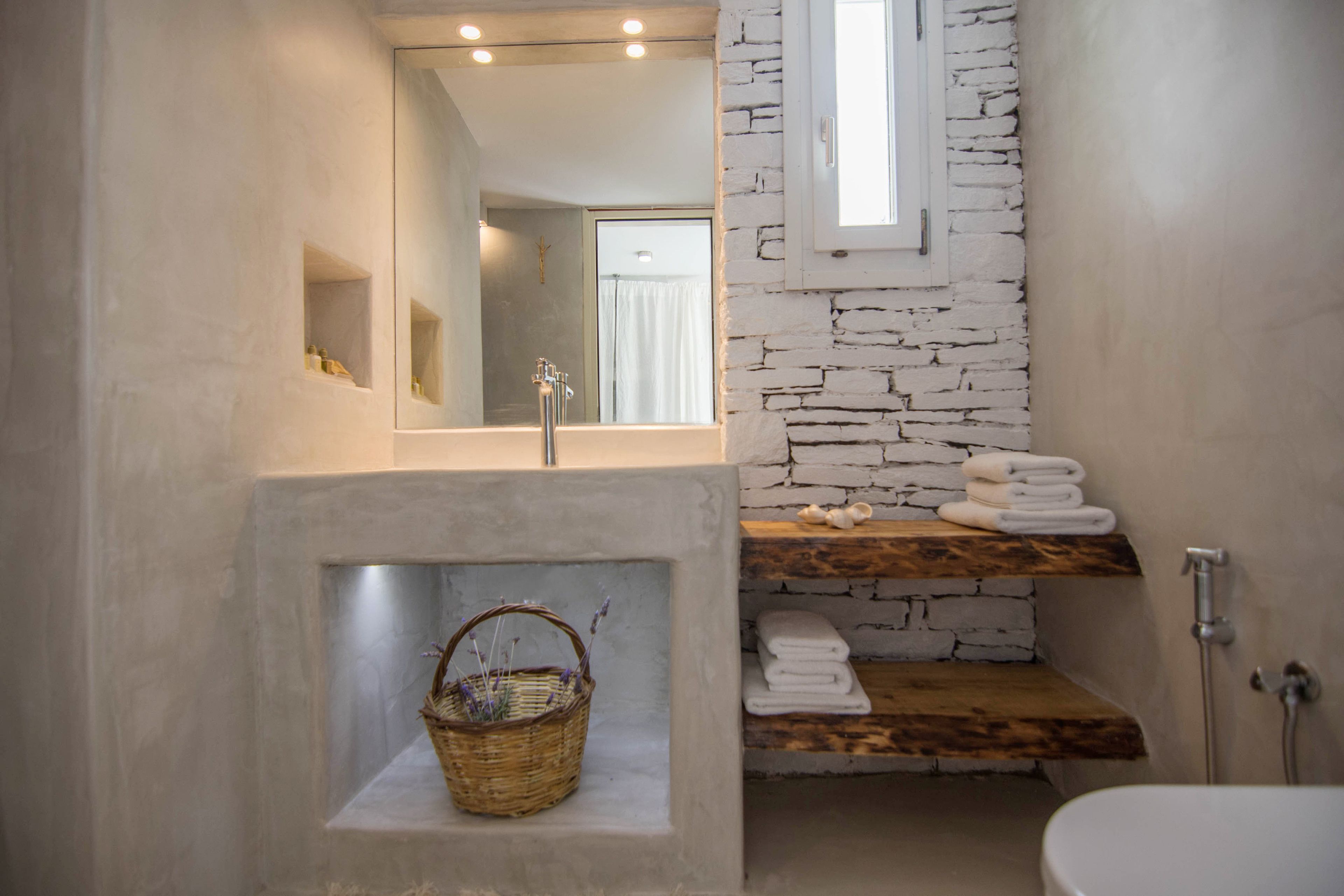 A bathroom with a stone wall, a wooden shelf with towels, a mirror, and a basket.