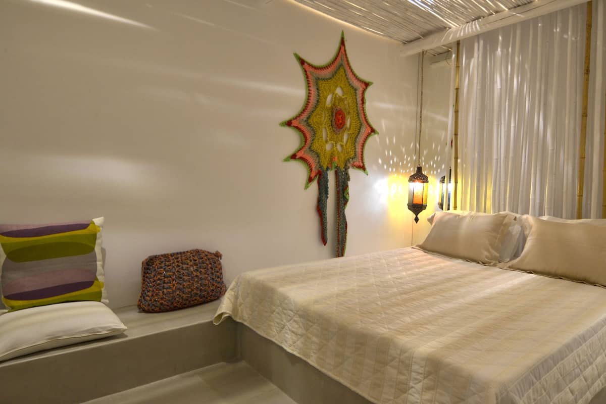 Un dormitorio con cama, almohadas, un tapiz y un banco con cojines.