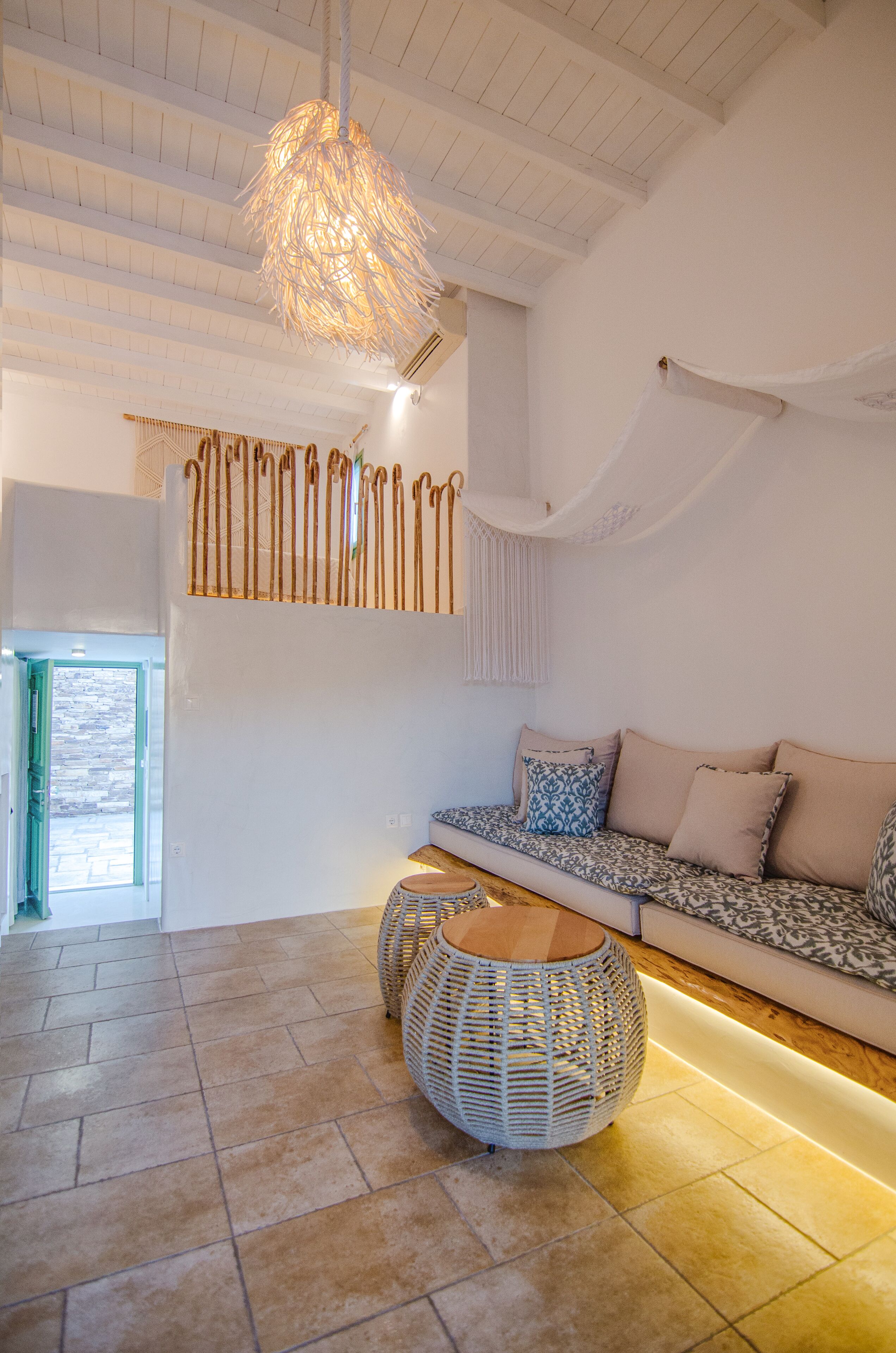 A modern interior with a wooden ceiling, a woven light fixture, a patterned sofa, and a round wicker table.
