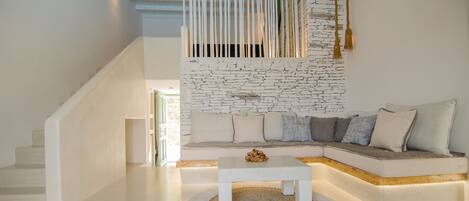 A modern living room with a white sofa, a small white coffee table, and a textured rug. A staircase with white railings leads to an upper level.