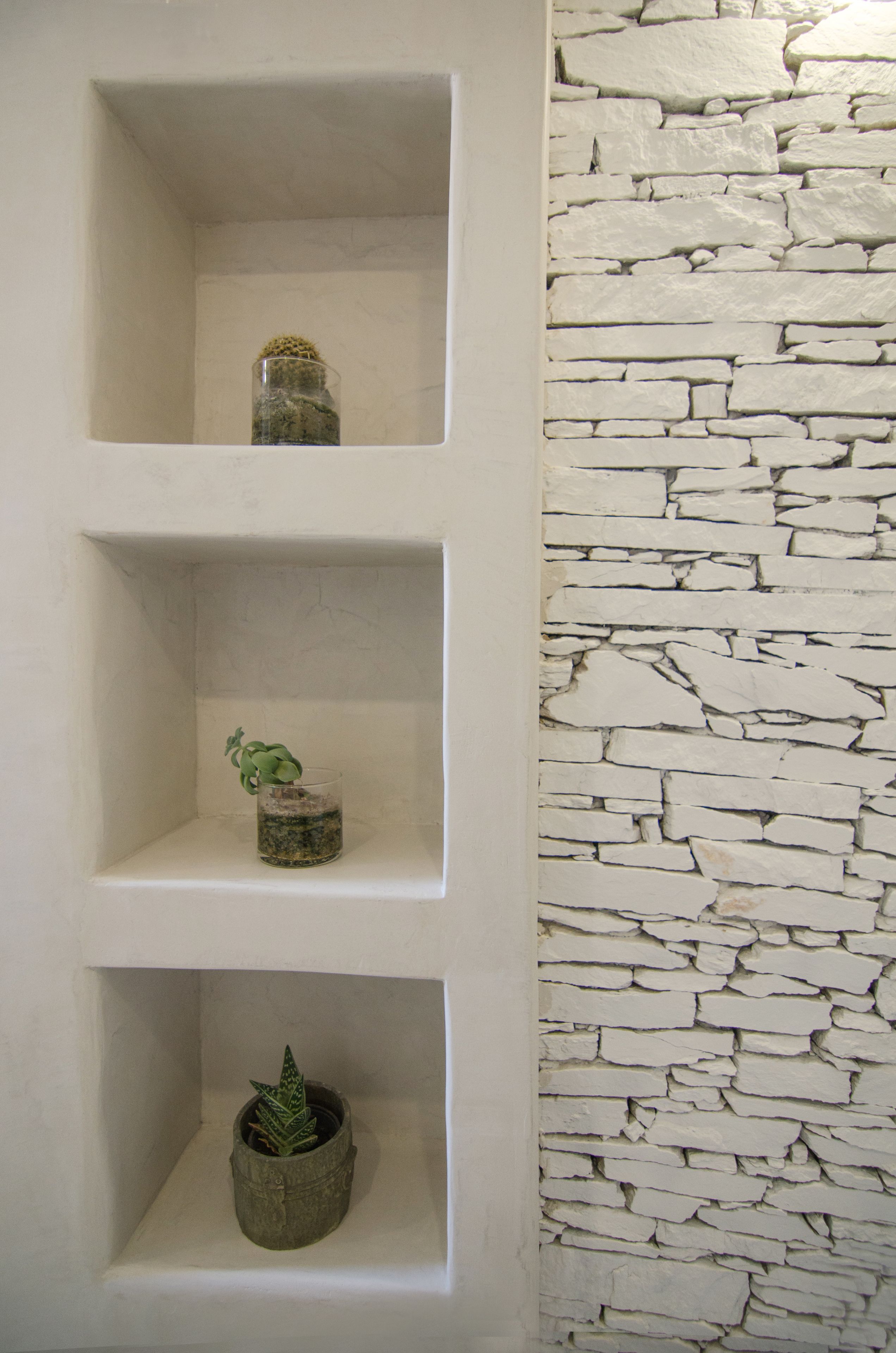 Three shelves with plants against a white wall with a stone pattern.