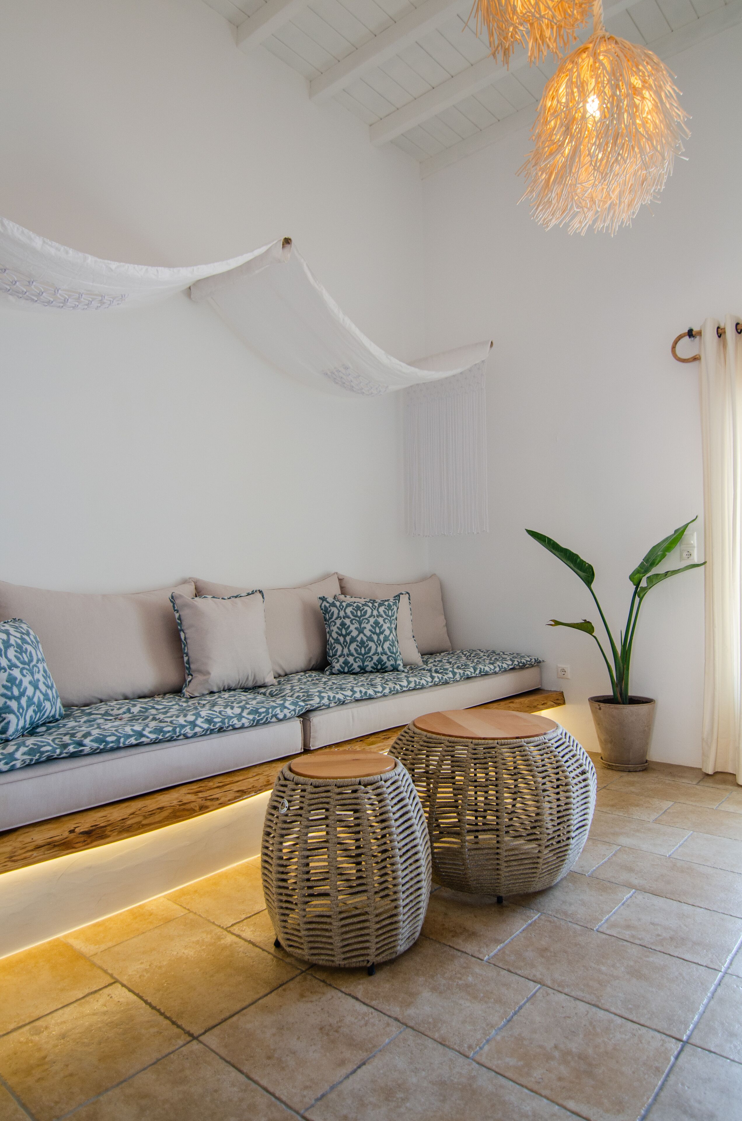 Un salon moderne avec un canapé, deux poufs en osier, une plante en pot et un luminaire suspendu.