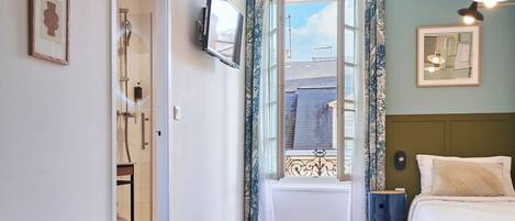 A hotel room with two beds, a TV mounted on the wall, a window with curtains, and a view of the outside.