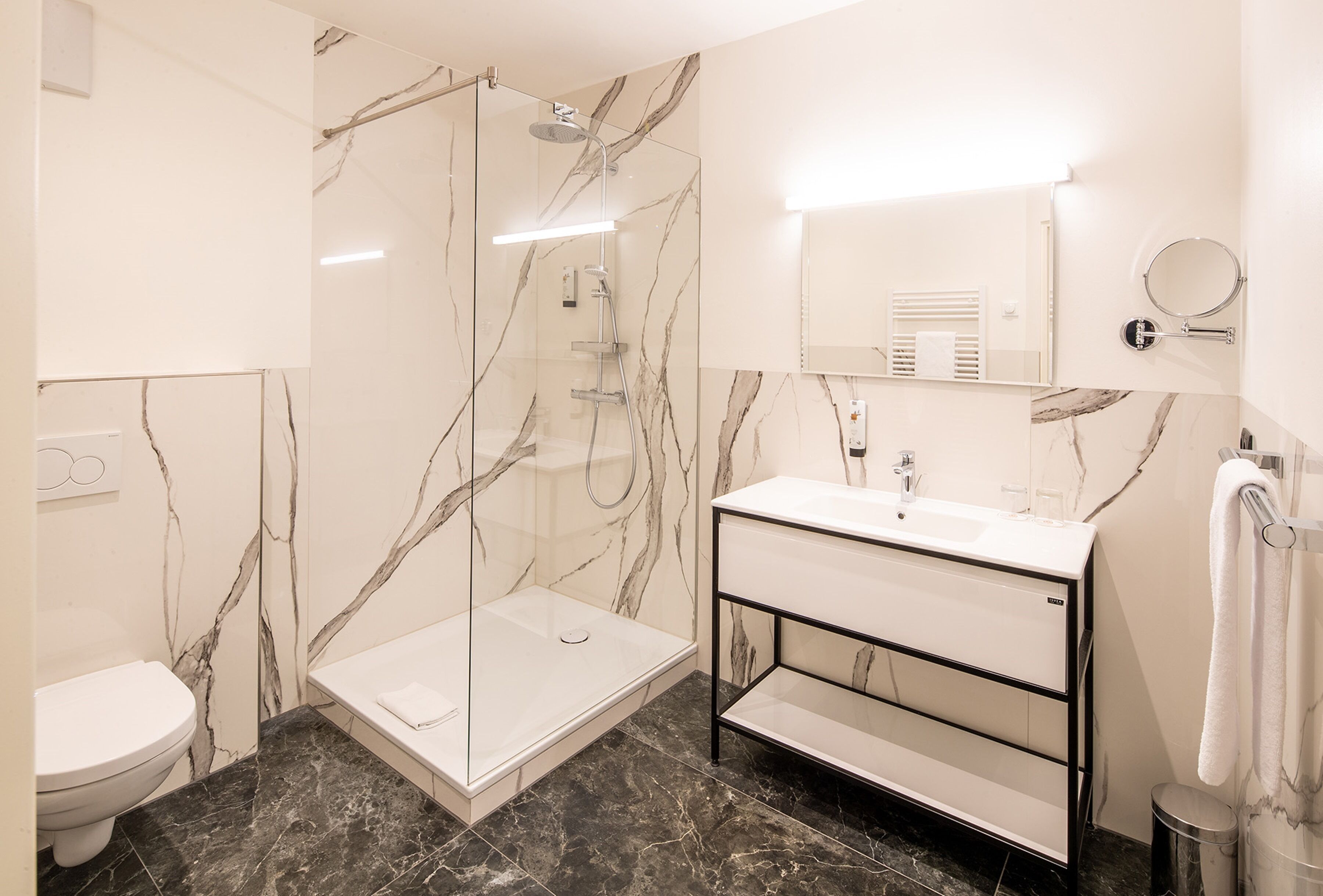 Une salle de bain moderne avec une douche à parois de verre, un lavabo blanc et un sol carrelé en marbre.