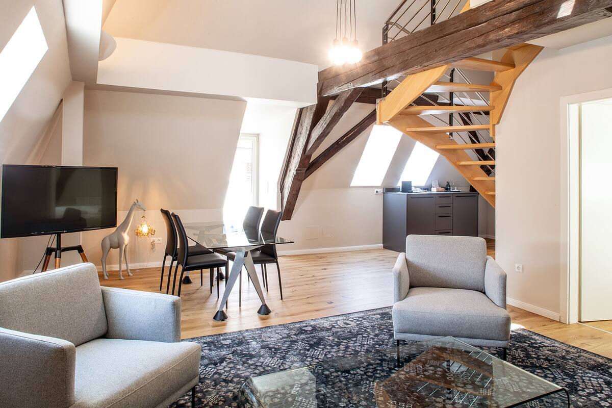 Een modern loft appartement met een eetgedeelte, twee banken, een televisie en een trap.