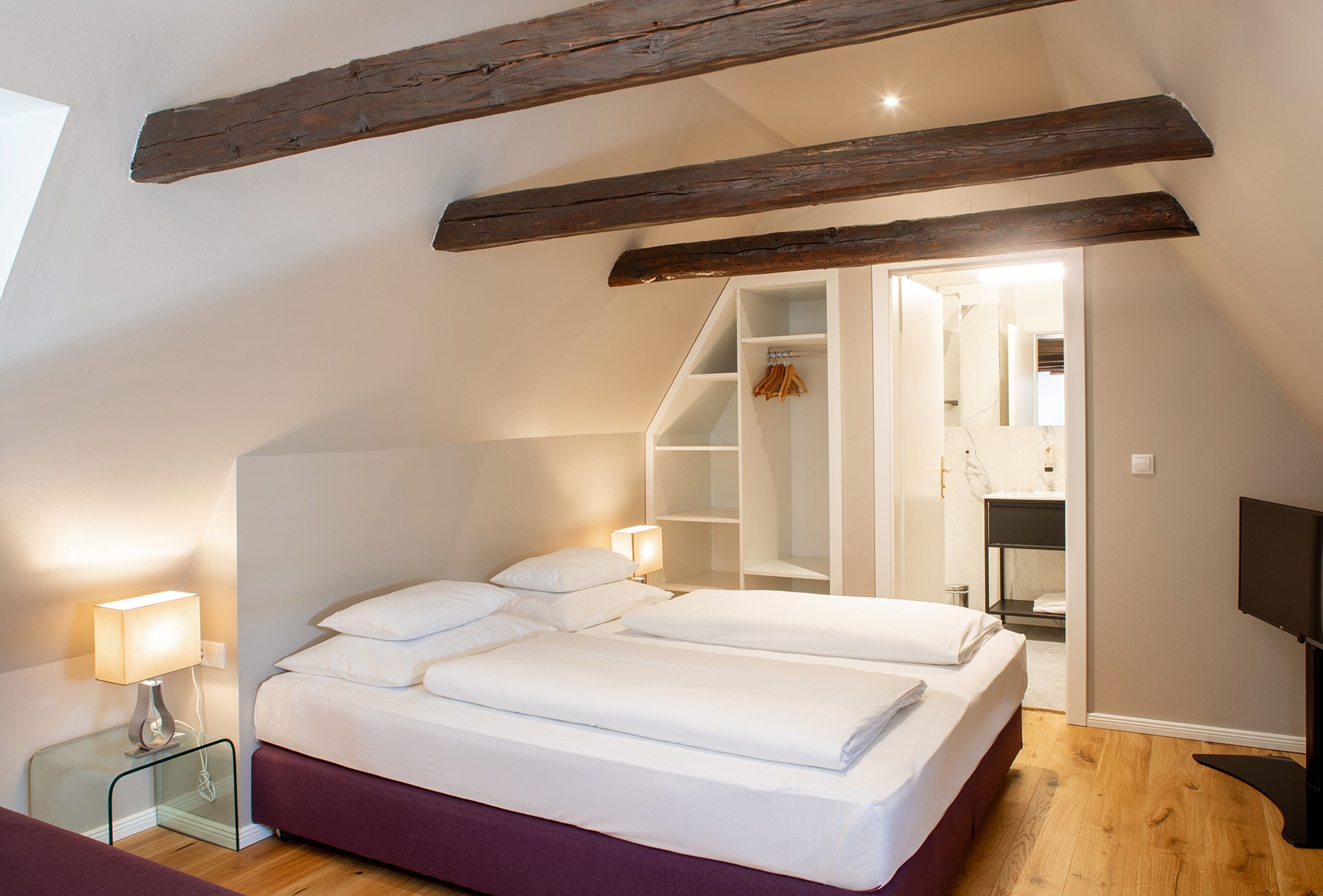 A bedroom with a large bed, a glass bedside table, a wardrobe, and a TV.