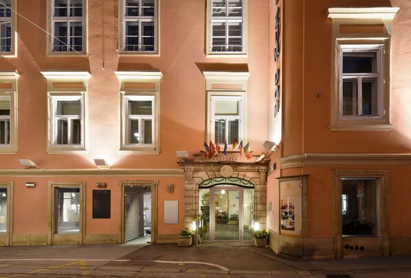 A hotel entrance with a central archway, multiple windows, and a flag display. - Boutique Hotel Dom - Rooms & Suites (Graz)