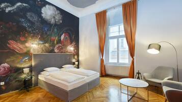 A bedroom with a large bed, a small round table, a chair, a lamp, and a floral mural on the wall.