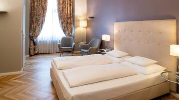 A hotel room with a large bed, two armchairs, a desk, and a lamp.