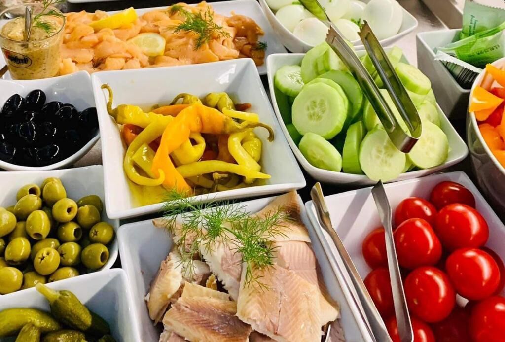 Una mesa con diversos alimentos, entre ellos vegetales en vinagre, aceitunas y pescado.