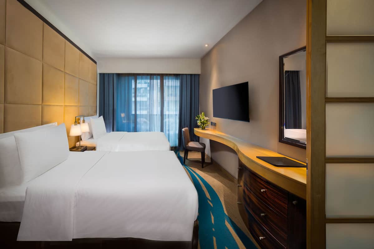 A hotel room with two beds, a desk with a flat-screen TV, a chair, and a large mirror.