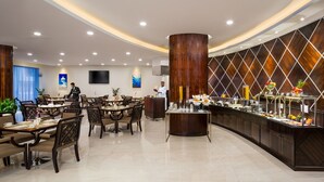 A modern hotel dining area with multiple tables and chairs, a buffet counter, and a large wooden column.