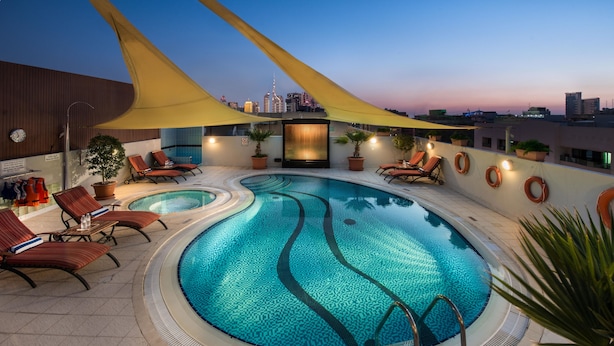 A rooftop pool with lounge chairs, potted plants, and a city skyline view.