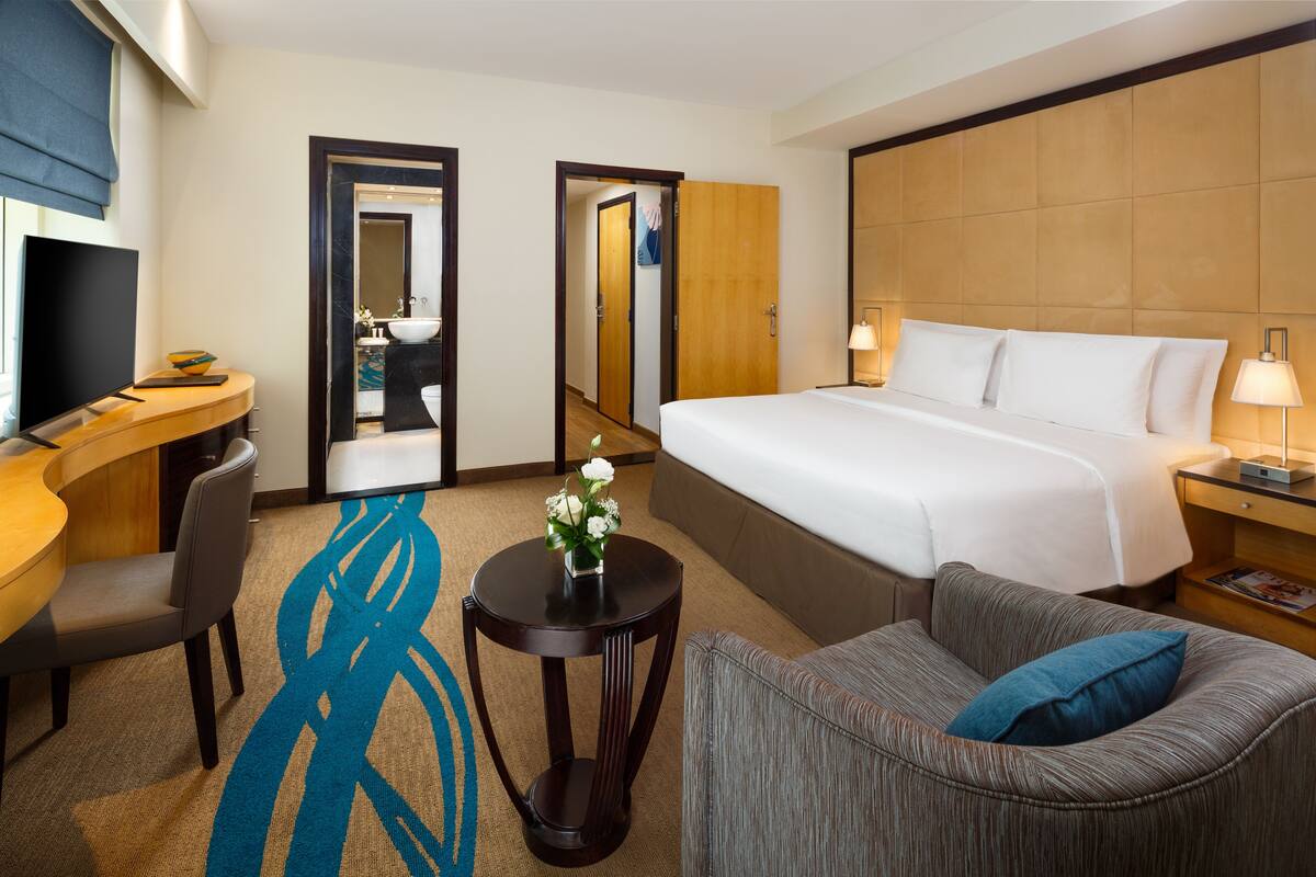 A hotel room with a bed, a desk with a chair, a sofa, a small table with a vase, and a mirror.