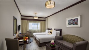 Habitación de hotel con dos camas, un sofá, una mesa de comedor con fruta, un televisor y una obra de arte enmarcada en la pared.