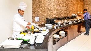 Montaje de bufé con varias estaciones de servicio, un chef preparando alimentos y una variedad de platos expuestos en la barra.