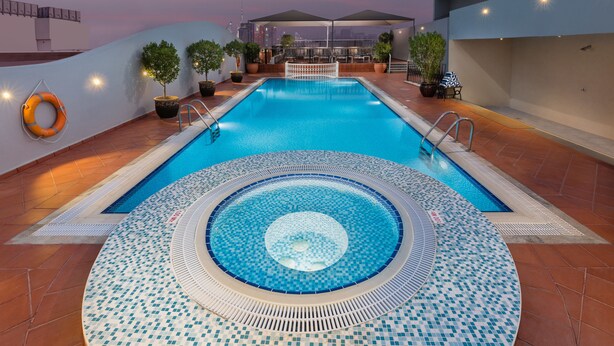 Una piscina en la azotea con un jacuzzi circular, plantas en macetas y vistas al horizonte de la ciudad.