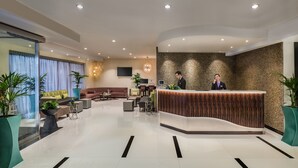 Un moderno vestíbulo de hotel con mostrador de recepción, zona de estar y un amplio ventanal con cortinas.