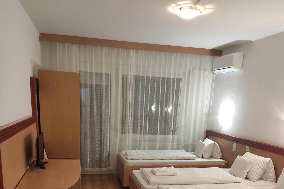 Habitación de hotel con dos camas, un escritorio y un amplio ventanal con cortinas translúcidas.