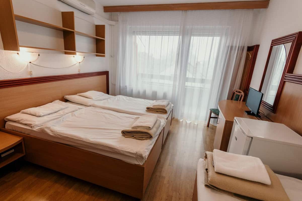 Una habitación de hotel con una cama de madera, un escritorio con computadora y un refrigerador pequeño.