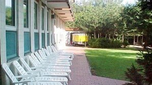 A row of white lounge chairs on a brick pathway leading to a building with large windows. - Tisza Sport Hotel (Szeged)