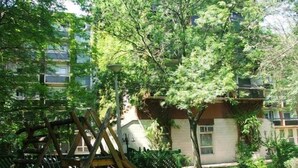 A playground with a slide and swings, surrounded by trees and a building with multiple windows. - Tisza Sport Hotel (Szeged)