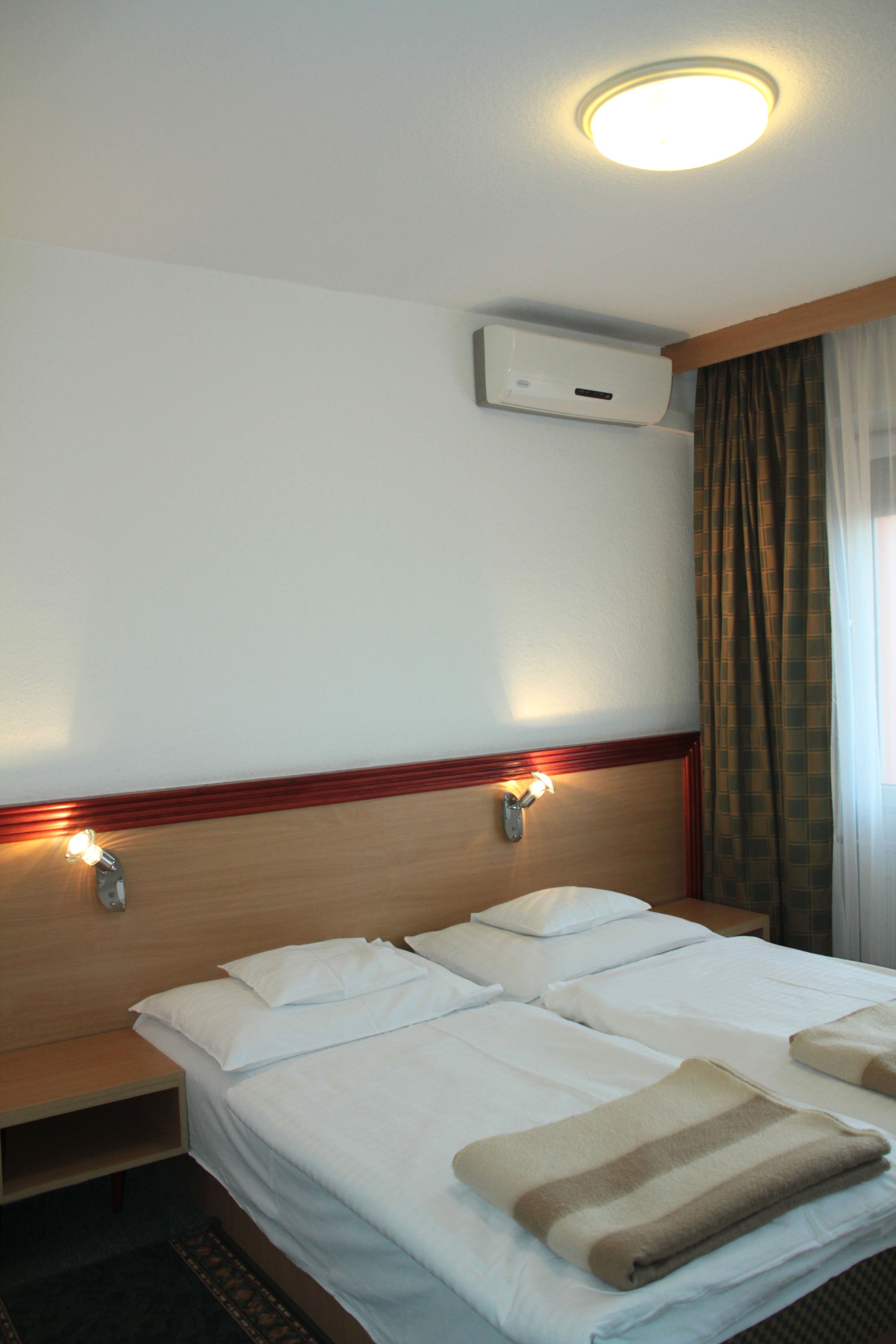 Habitación de hotel con una cama grande, dos mesitas de noche, aire acondicionado de pared y una ventana con cortinas.