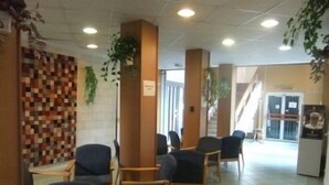 A reception area with a check-in counter, seating area with chairs, and a tiled floor. - Tisza Sport Hotel (Szeged)