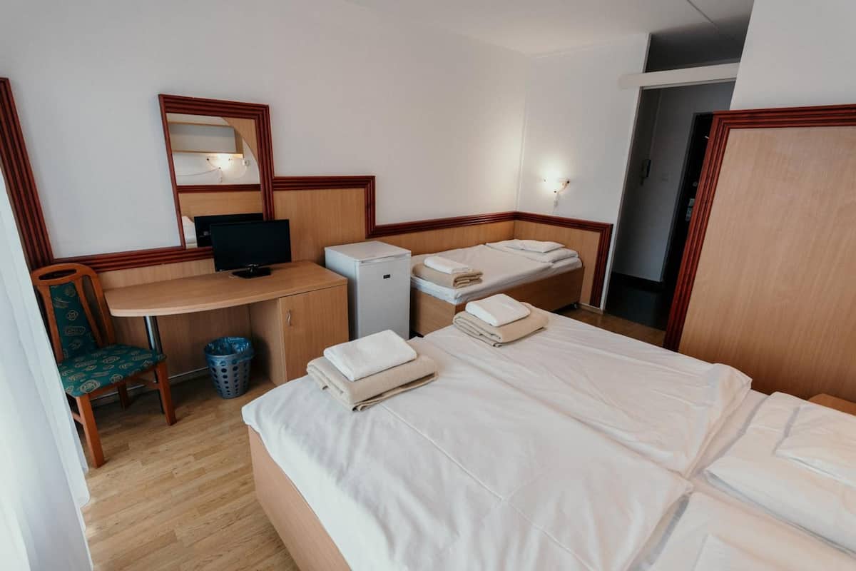 Una habitación de hotel con un escritorio de madera, una computadora, un televisor, dos camas y una silla.