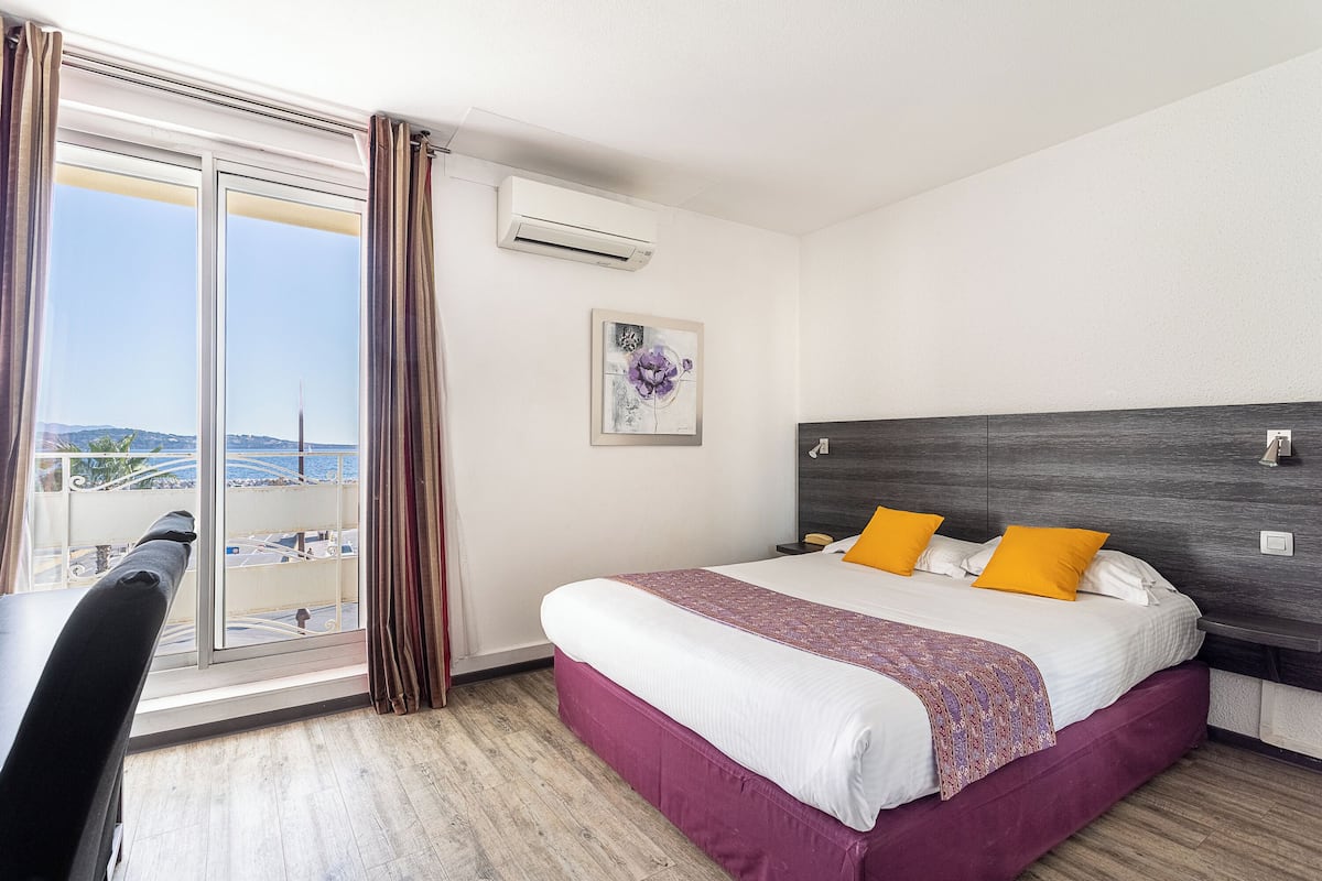 A hotel room with a large bed, a desk, and a view of the sea.